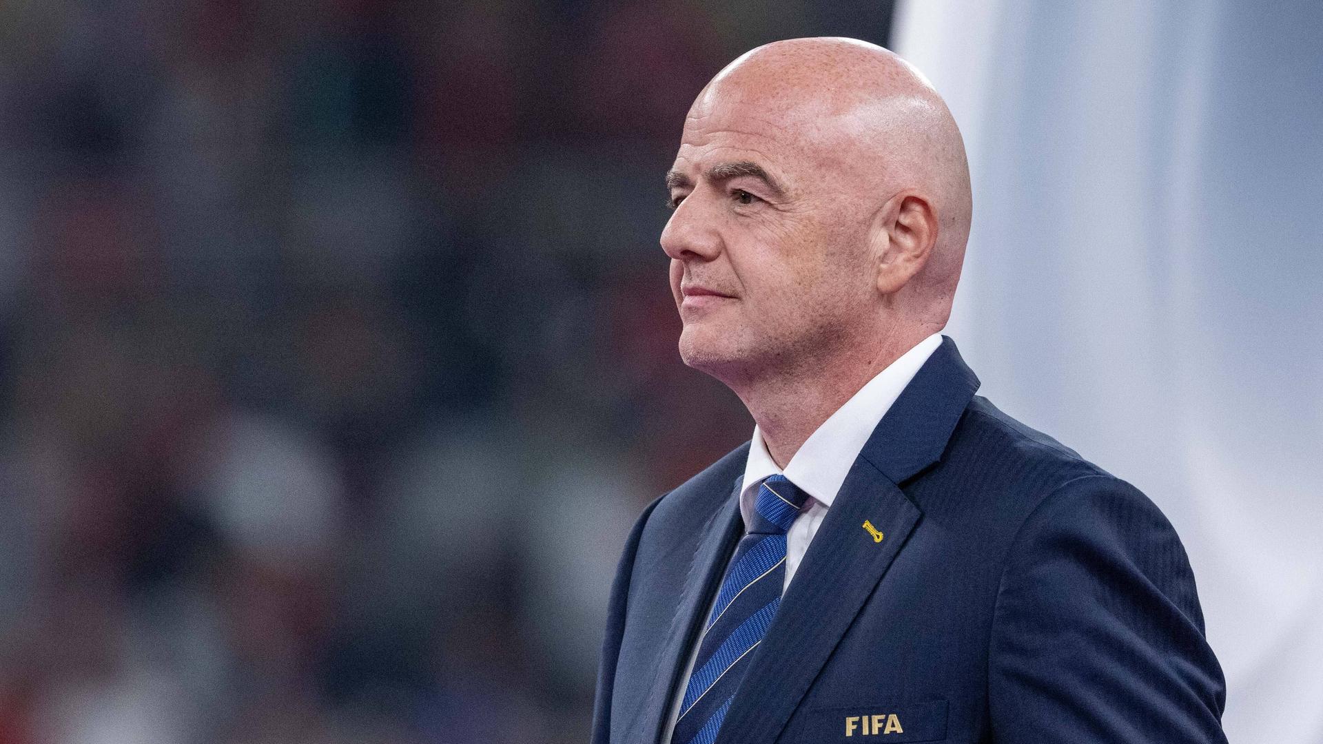 Gianni Infantino steht bei einem WM-Spiel im Anzug auf dem Rasen.