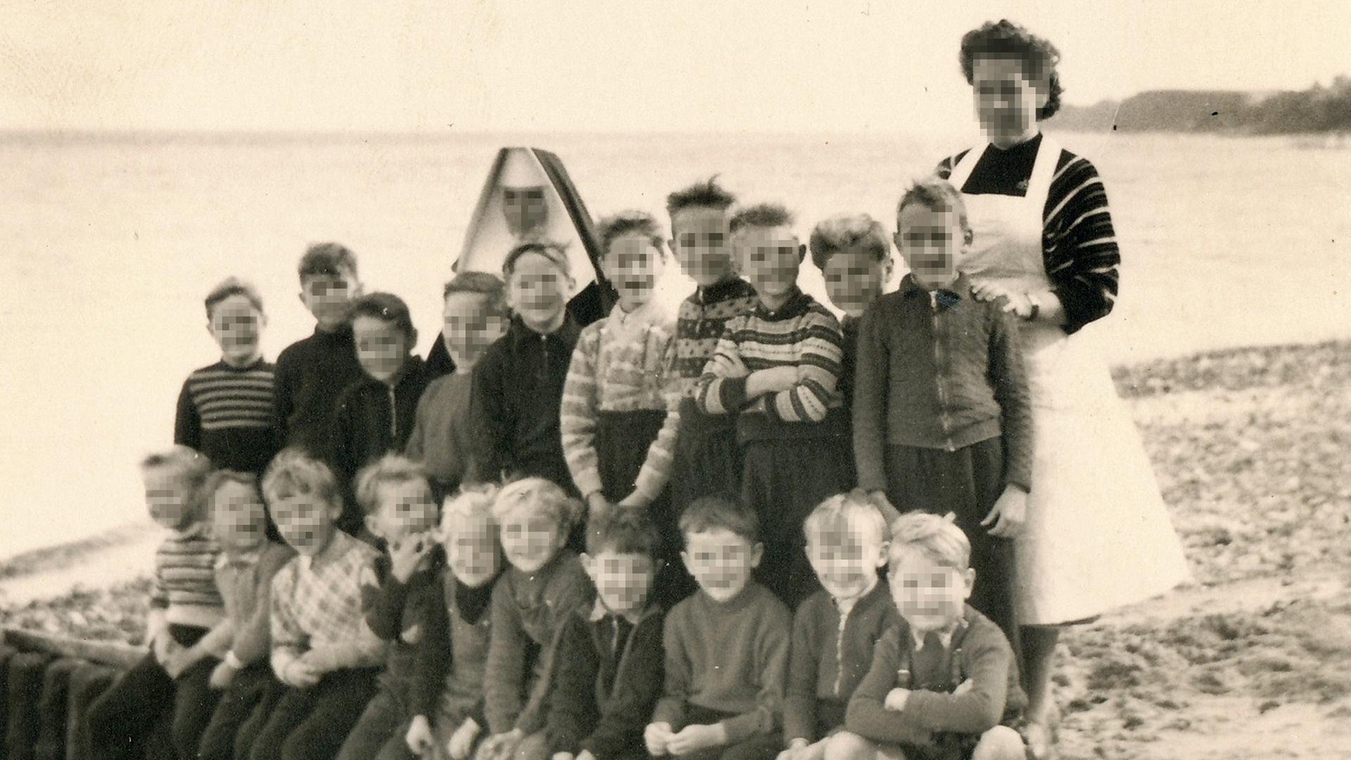 Ein altes Gruppenfoto zeigt eine Gruppe von Kindern mit ihren beiden Betreuerinnen in Niendorf am Strand. Die Gesichter sind verpixelt.