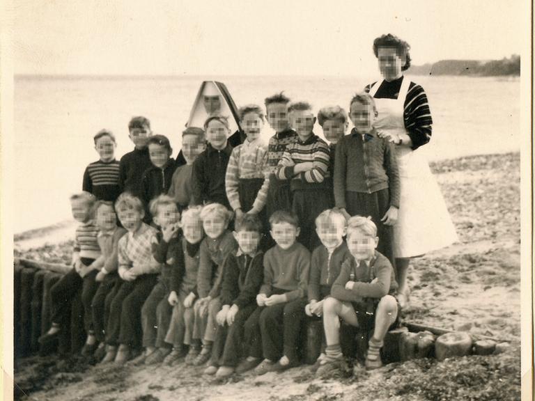 Ein altes Gruppenfoto zeigt eine Gruppe von Kindern mit ihren beiden Betreuerinnen in Niendorf am Strand. Die Gesichter sind verpixelt.