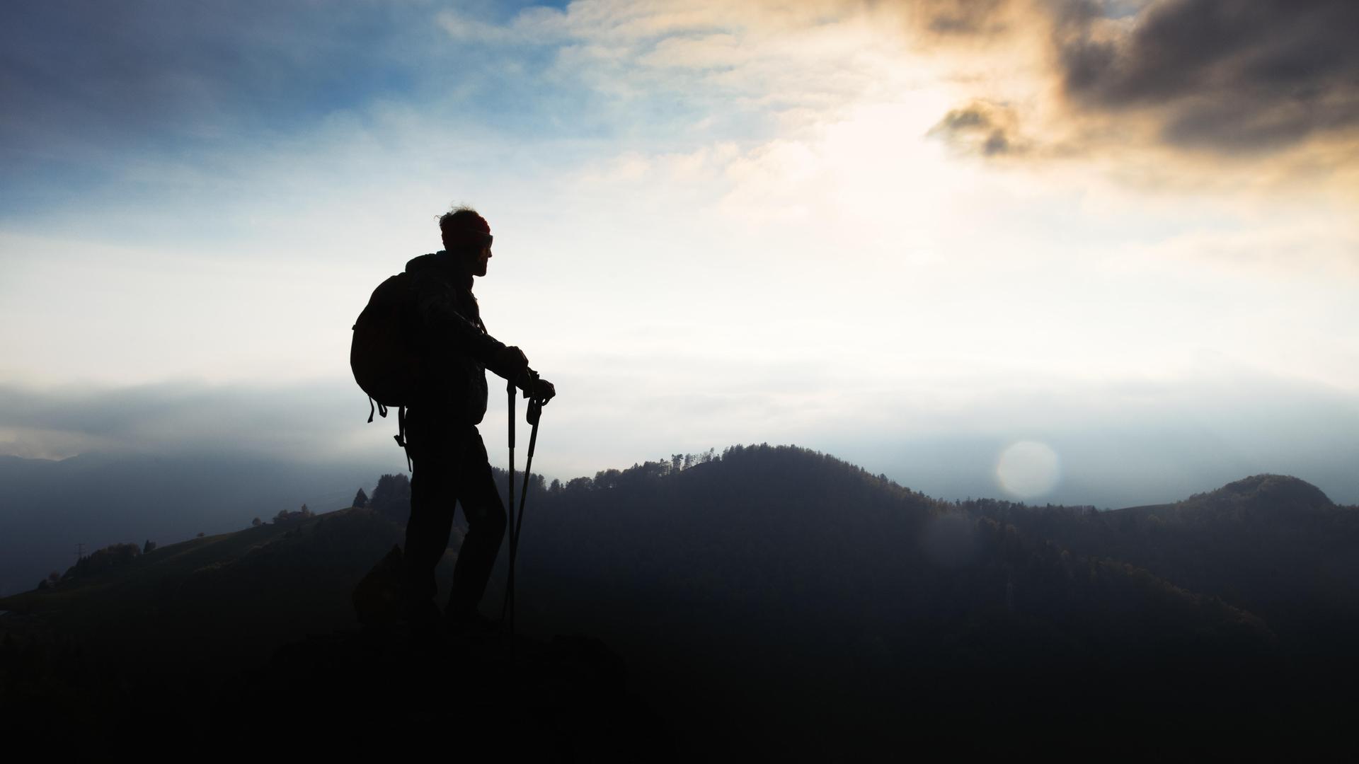 Ein Mann mit Walking-Stöcken steht auf einem Berg bei Sonnenuntergang