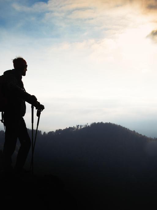 Ein Mann mit Walking-Stöcken steht auf einem Berg bei Sonnenuntergang