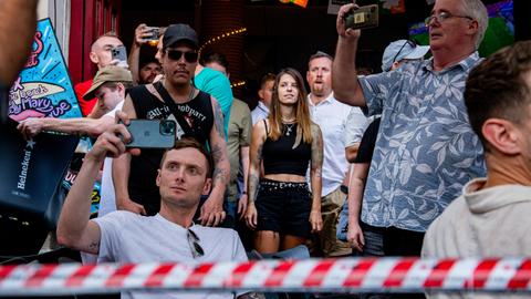 Am Rande eines Protests gegen zu viele Touristen in Barcelona, fotografieren Touristen die Protestierenden, hinter rot-weißem Absperrband.