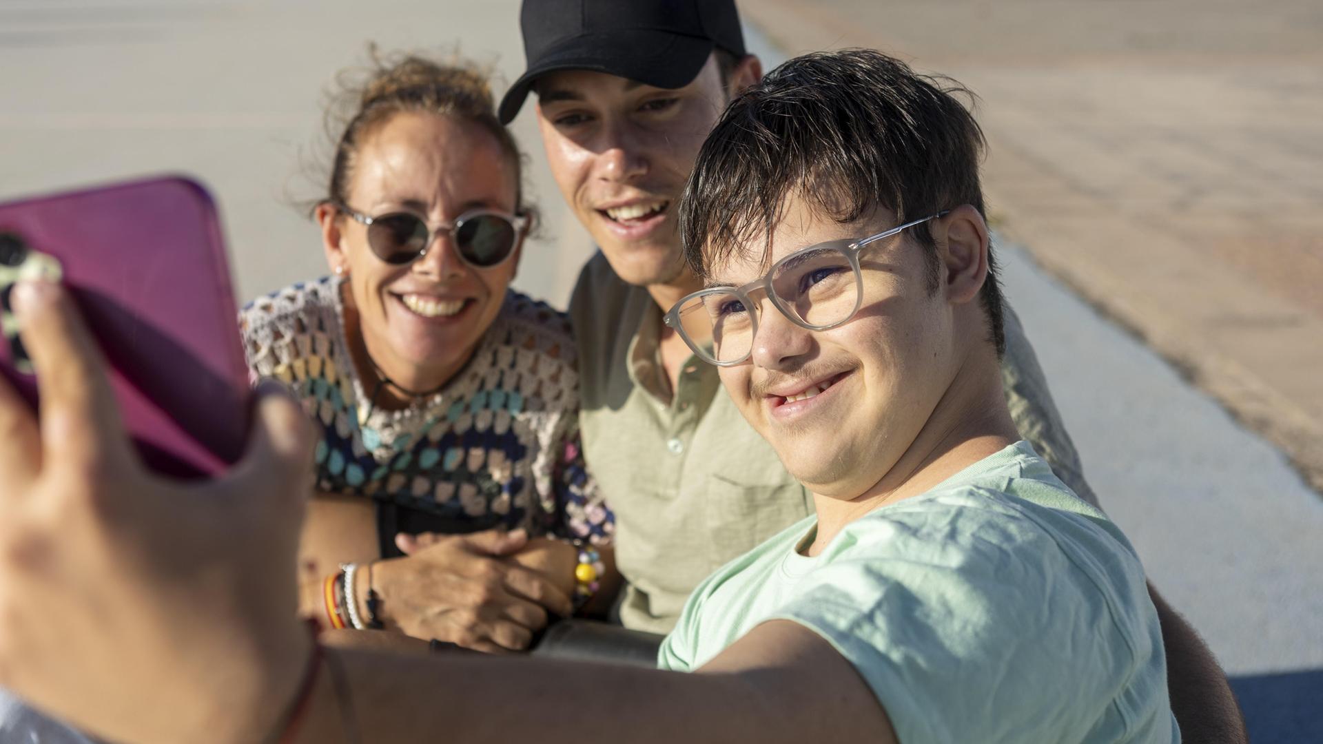 Drei Menschen machen mit einem Handy ein Selfie. Ein Mann hat das Down-Syndrom.