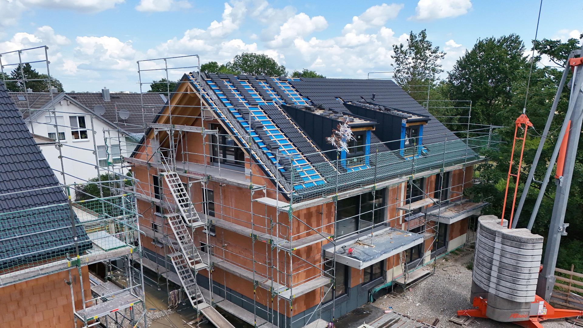 Das Dach eines Mehrfamilienhauses im Rohbau ist fast eingedeckt.