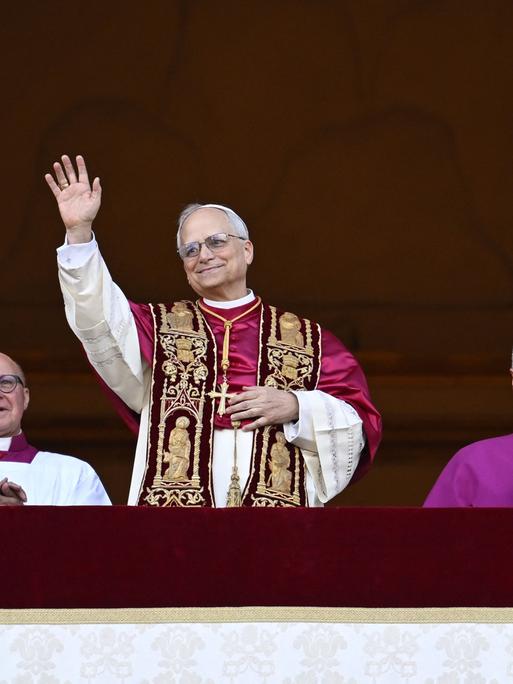 Der neu gewählte Papst, Leo XIV, steht auf dem Balkon des Petersdoms im Vatikan am 8. Mai 2025. Seine Hände sind gefaltet und er hat ein Lächeln auf den Lippen - Er scheint sichtlich glücklich über sein neues Amt. 