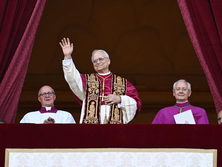 Der neu gewählte Papst, Leo XIV, steht auf dem Balkon des Petersdoms im Vatikan am 8. Mai 2025. Seine Hände sind gefaltet und er hat ein Lächeln auf den Lippen - Er scheint sichtlich glücklich über sein neues Amt. 