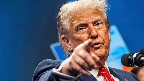 Trump steht an einem Rednerpult und zeigt mit seinem Finger nach vorne. 