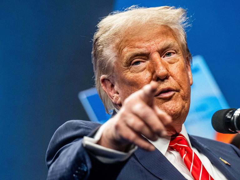 US-Präsident Trump steht an einem Rednerpult und zeigt mit seinem Finger nach vorne. 