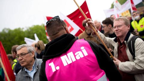 Ein Mann trägt während einer Kundgebung eine Warnweste mit dem Aufdruck "1. Mai".