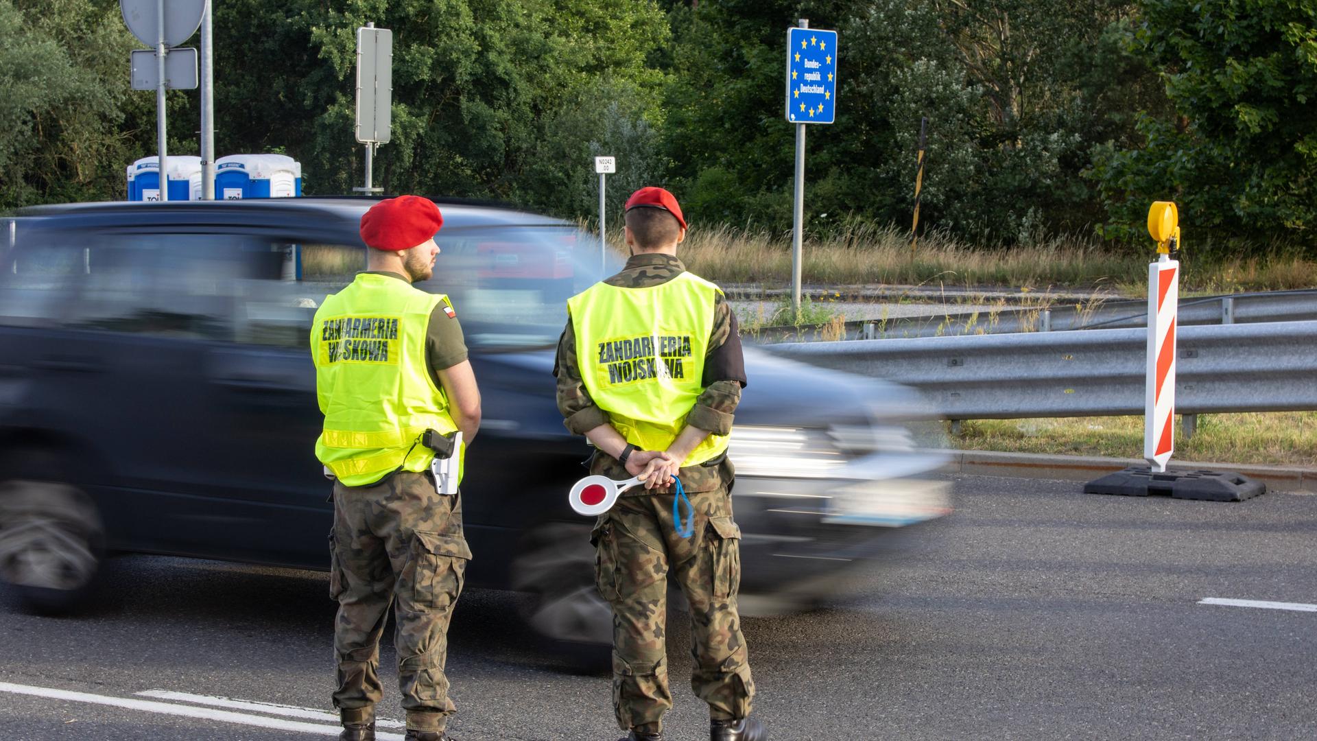 Polnische Beamte stehen an einer Straße vor der Grenze und kontrollieren Autos. Polnische Beamte stehen an einer Straße vor der Grenze und kontrollieren Autos.