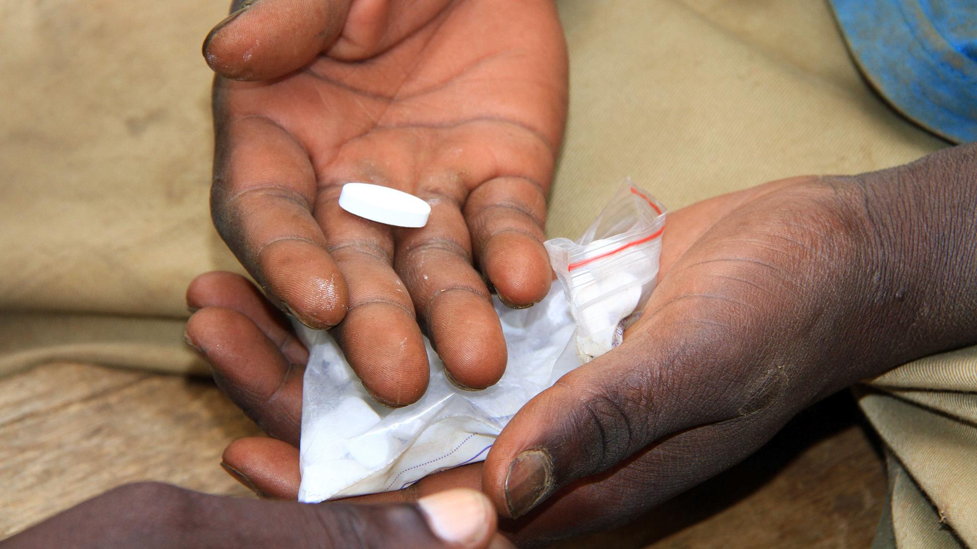 Zwei offene Hände halten eine weiße längliche Tablette und ein kleines Plastikbeutelchen mit weiteren Tabletten
