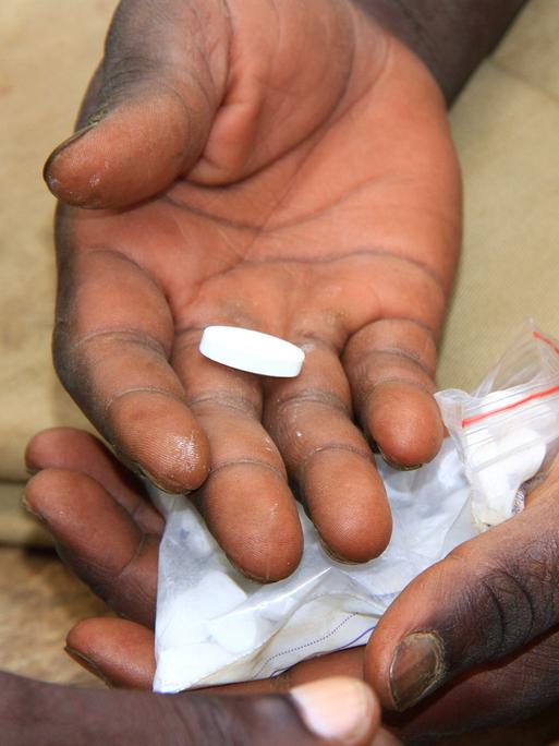 Zwei offene Hände halten eine weiße längliche Tablette und ein kleines Plastikbeutelchen mit weiteren Tabletten Zwei offene Hände halten eine weiße längliche Tablette und ein kleines Plastikbeutelchen mit weiteren Tabletten