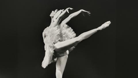 Schwarzweißfoto einer Ballerina im weißen Tanzkleid auf der Bühne.