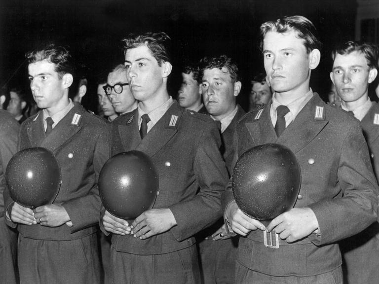 Historisches Schwarzweißfoto von Bundeswehrrekruten während der feierlichen Verpflichtung. Sie stehen aufgereiht nebeneinander und halten ihre Helme vor der Brust.