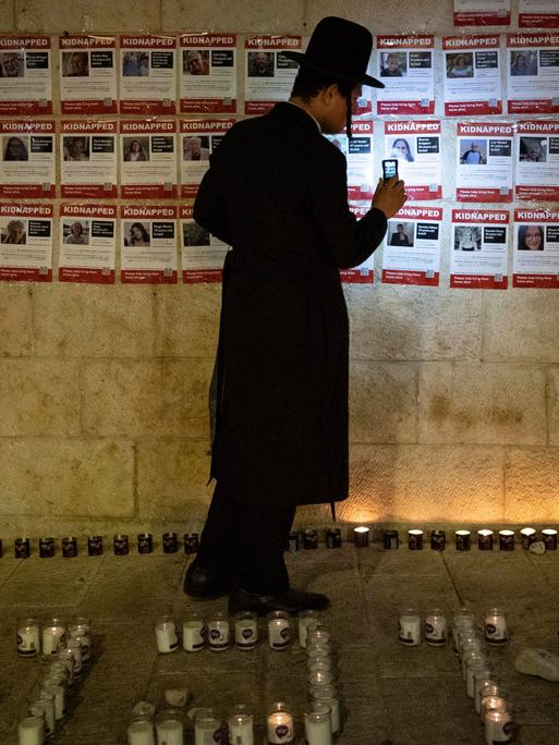 Ein Mann leuchtet mit seinem Smartphone Gesucht-Bilder mit den Geiseln der Hamas an.