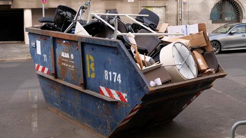 Alte Büromöbel, darunter viele Bürostühle, liegen in einem Container für Müll und Bauschutt, um entsorgt zu werden.