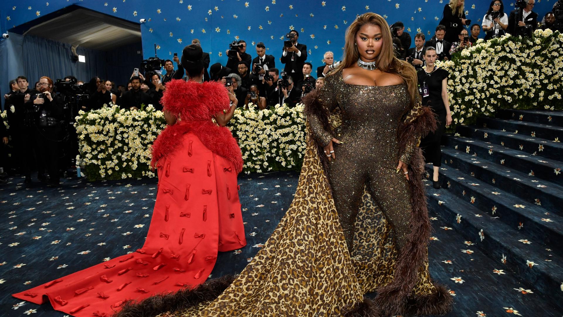 Precious Lee zeigt sich bei der Met Gala den Fotografen. Sie trägt einen engen Glitzeranzug und einen Umhang mit Leoparden-Muster. Neben ihr eine weitere Frau mit auslander roter Schleppe von hinten. Precious Lee zeigt sich bei der Met Gala den Fotografen. Sie trägt einen engen Glitzeranzug und einen Umhang mit Leoparden-Muster. Neben ihr eine weitere Frau mit auslander roter Schleppe von hinten.