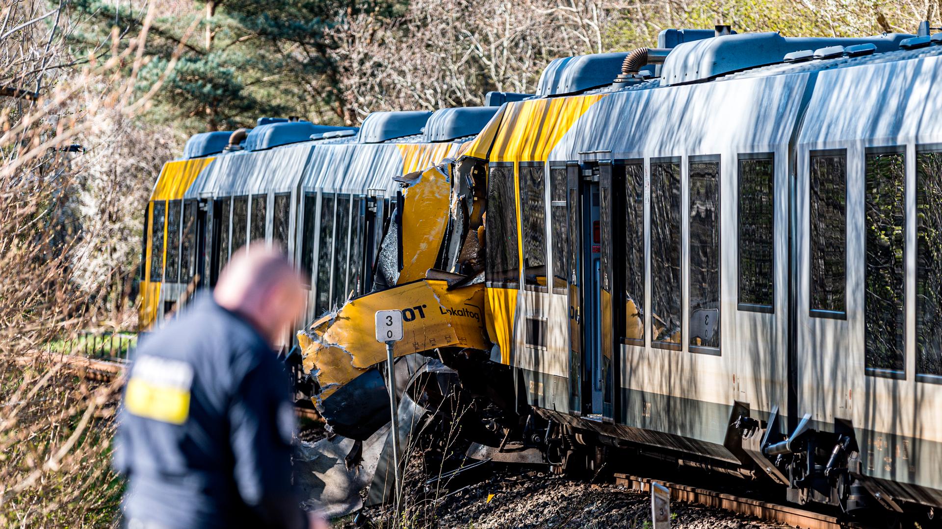 Zu sehen sind zwei kollidierte Regionalzüge - die Fronten sind eingedrückt. Im Vordergrund steht unscharf ein Polizist.