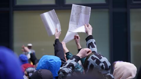 Flüchtlinge halten Formulare in einer Warteschlange vor einer Ausländerbehörde hoch.
