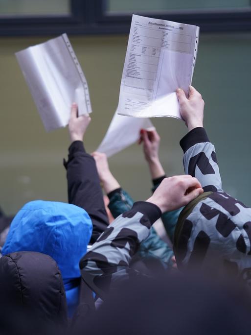 Flüchtlinge halten Formulare in einer Warteschlange vor einer Ausländerbehörde hoch.