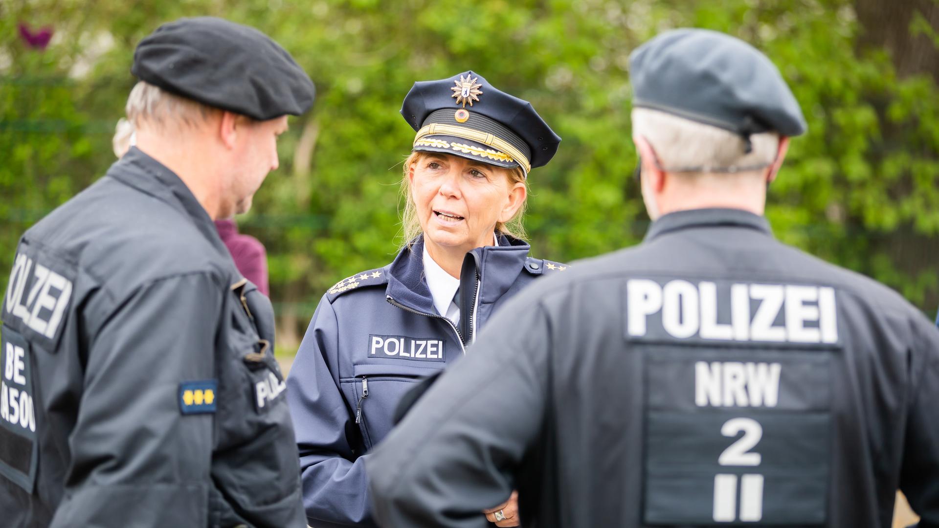 Berlins Polizeipräsidentin Barbara Slowik unterhält sich am Rande einer Kundgebung uniformiert mit zwei Polzisten.