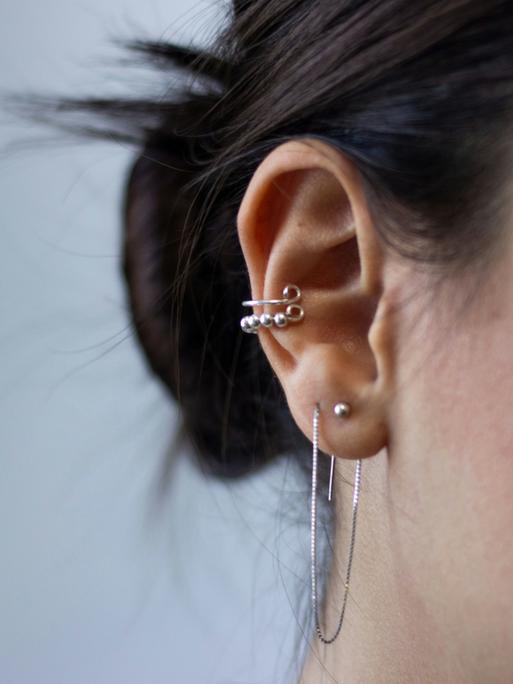 Großaufnahme eines Ohres einer jungen Frau, die viel Silberschmuck am Ohr trägt.