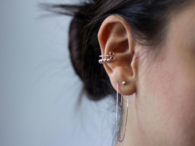 Großaufnahme eines Ohres einer jungen Frau, die viel Silberschmuck am Ohr trägt.
