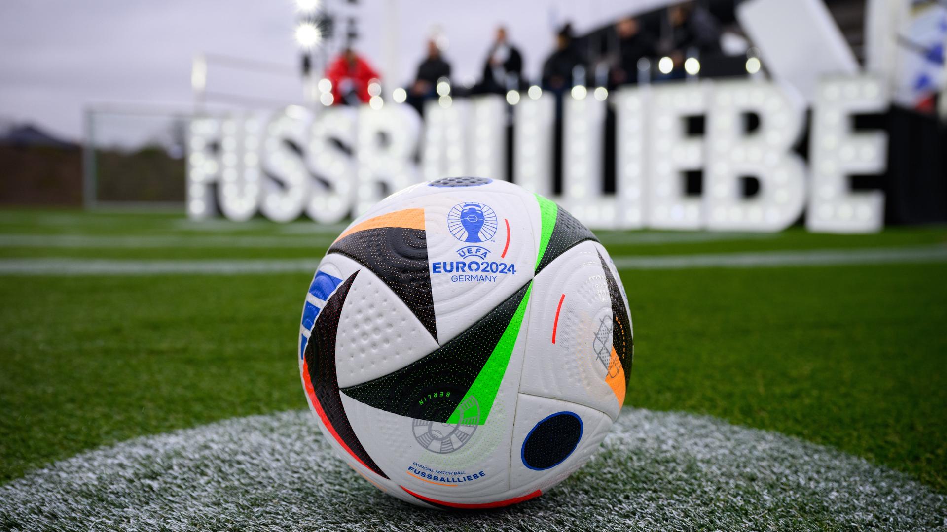 Der neue Fußball liegt bei der Vorstellung des EM-Spielballs für die UEFA EURO 2024 auf dem Maifeld am Olympiastadion. Im Hintergrund sieht verschwommen in großen weißen Lettern den Namen "Fussballliebe".
