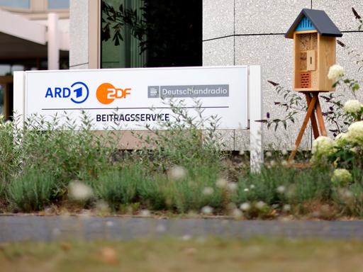 Ein Schild mit der Aufschrift "Beitragsservice" steht vor dem Eingang des Beitragsservice auf dem WDR-Gelände in Köln Bocklemünd. 