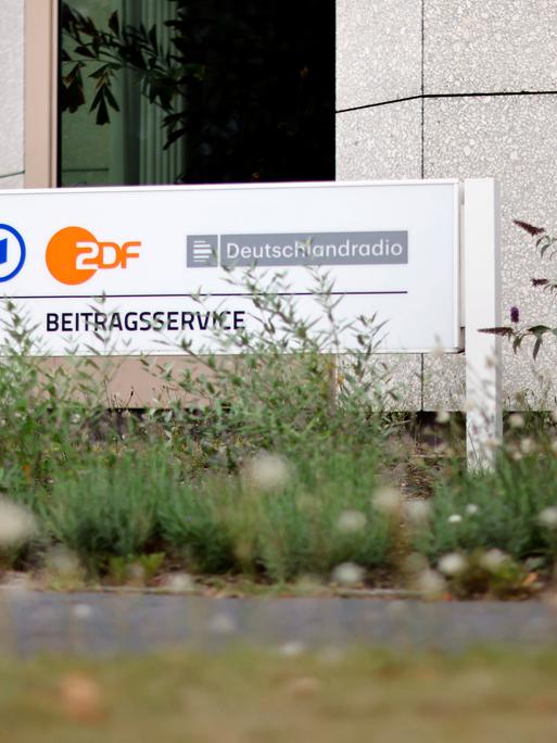 Ein Schild mit der Aufschrift "Beitragsservice" steht vor dem Eingang des Beitragsservice auf dem WDR-Gelände in Köln Bocklemünd. 