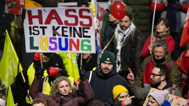 Eine Demonstrantin trägt ein Schild. Darauf steht "Hass ist keine Lösung". Neben ihr stehen noch viele andere Demonstranten.