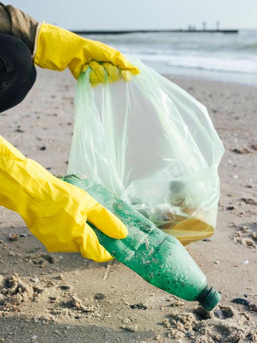 Eine Person sammlt Plastikmüll am Strand. 