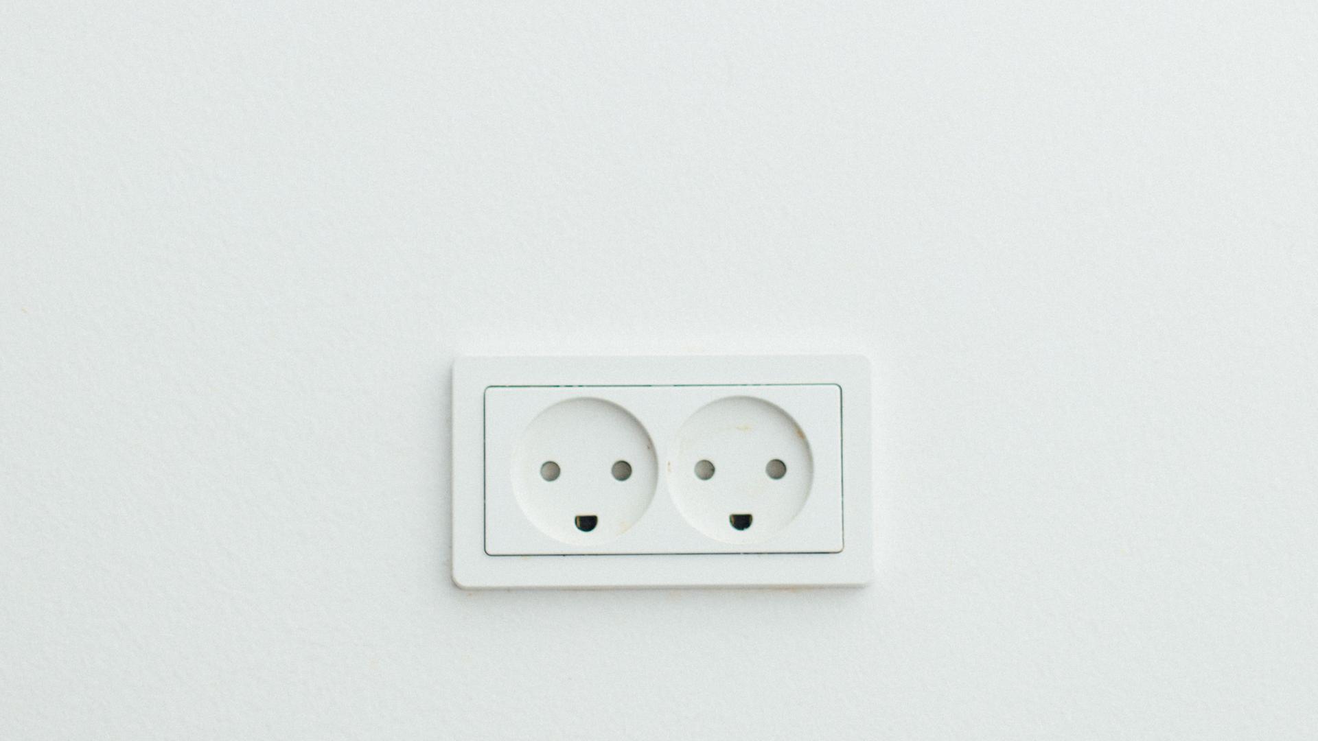 Eine Doppelsteckdose auf weißer Wand. Sie erinnert an Smileys.