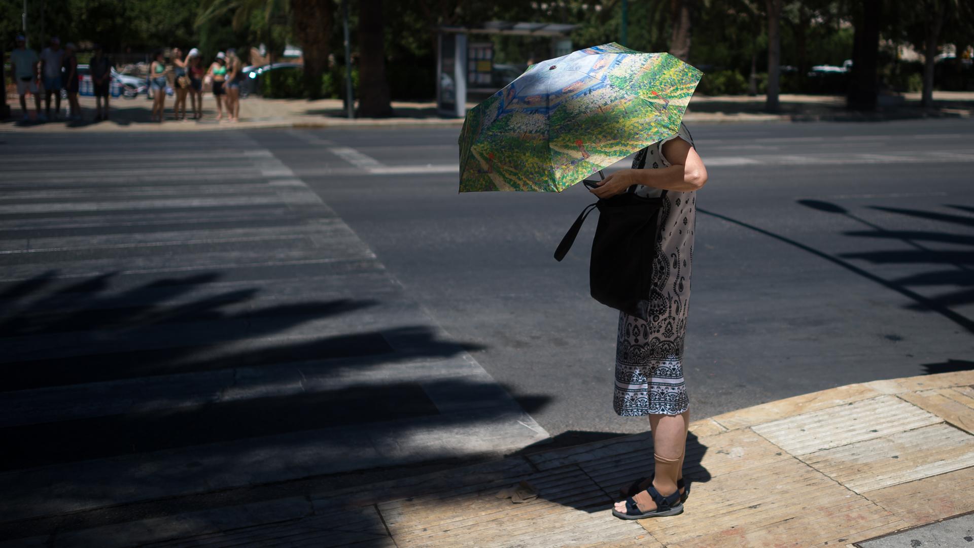 Eine Frau schützt sich auf einer Straße stehend mit einem Sonnenschirm vor der Sonne. Eine Frau schützt sich auf einer Straße stehend mit einem Sonnenschirm vor der Sonne.