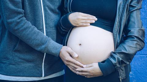 Symbolbild: Eine junge, schwangere Frau hält ihren Bauch unter einem kurzen Top.