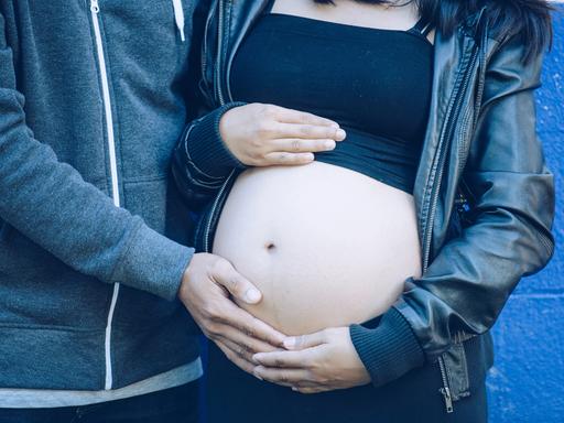 Symbolbild: Eine junge, schwangere Frau hält ihren Bauch unter einem kurzen Top.