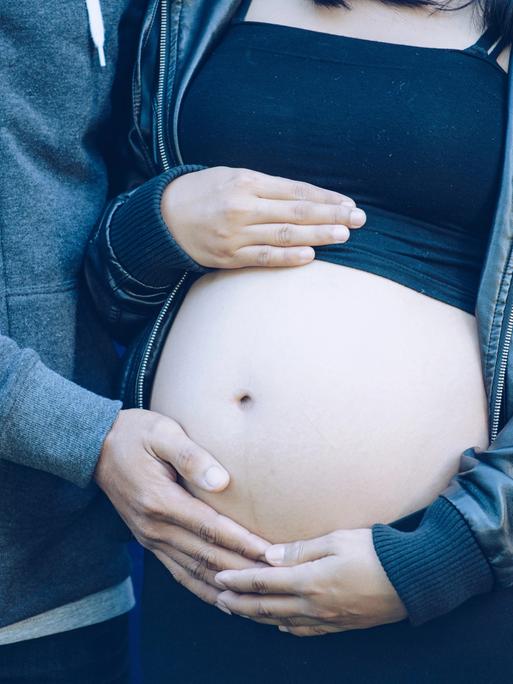 Symbolbild: Eine junge, schwangere Frau hält ihren Bauch unter einem kurzen Top.