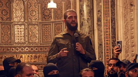 Der Rebellenführer Abu Mohammed al-Dschulani spricht in der Umayyaden-Moschee von Damaskus in ein Mikrofon zu einer Gruppe von Menschen.