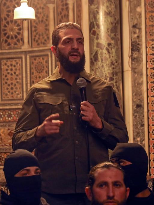 Der Rebellenführer Abu Mohammed al-Dschulani spricht in der Umayyaden-Moschee von Damaskus in ein Mikrofon zu einer Gruppe von Menschen.