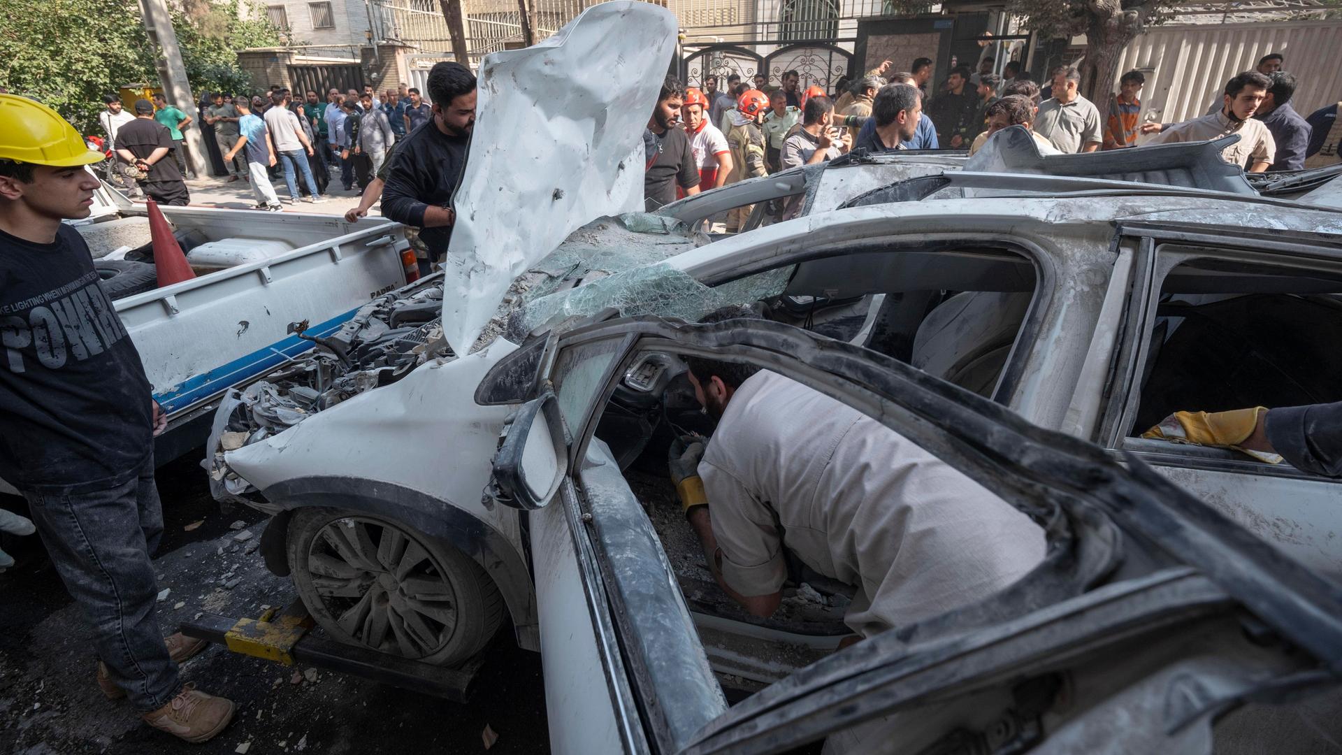 Hilfskräfte und Umstehende blicken auf ein völlig zerstörtes Auto.