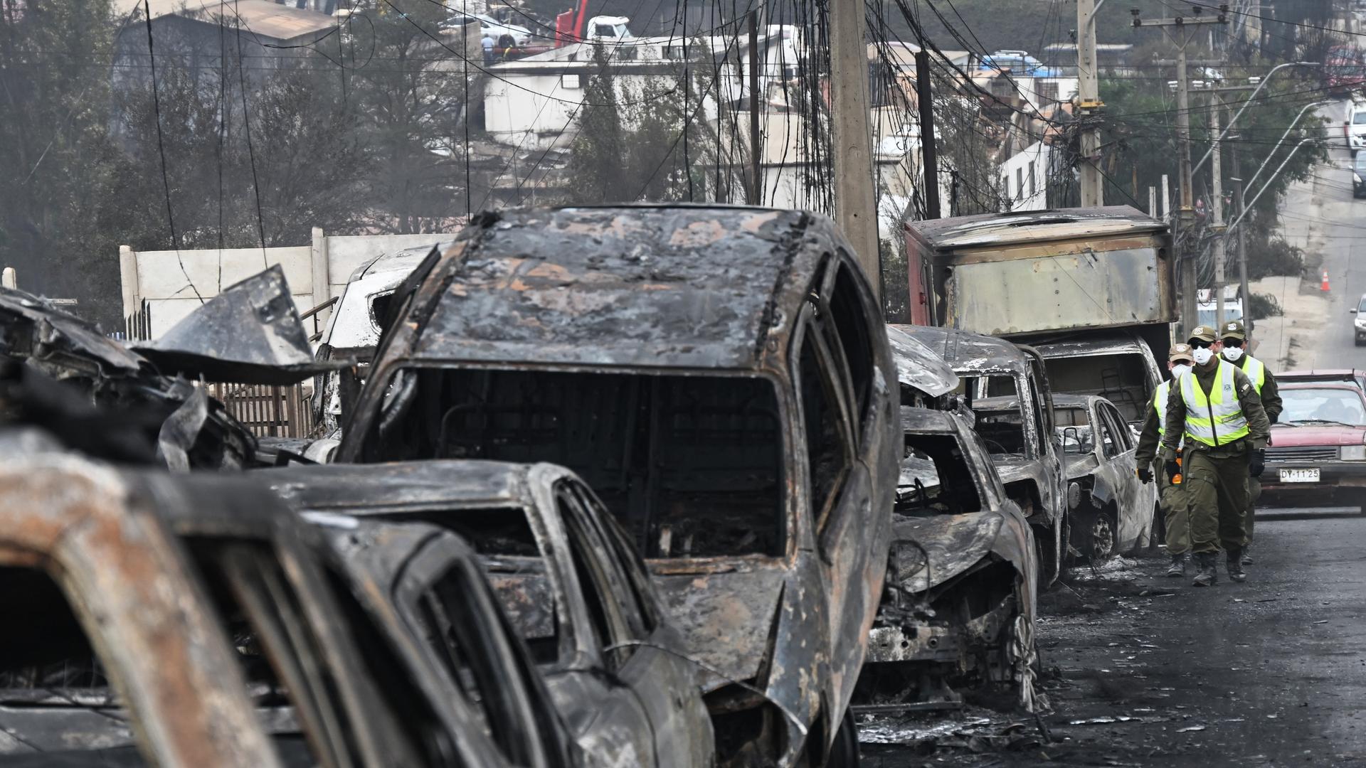 Einsatzkräfte in Chile gehen an einer Reihe völlig zerstörter Autos vorbei.
