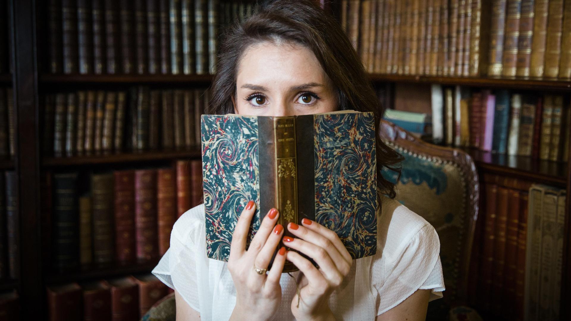 Eine Frau schaut hinter einem aufgeschlagenen Buch hervor.