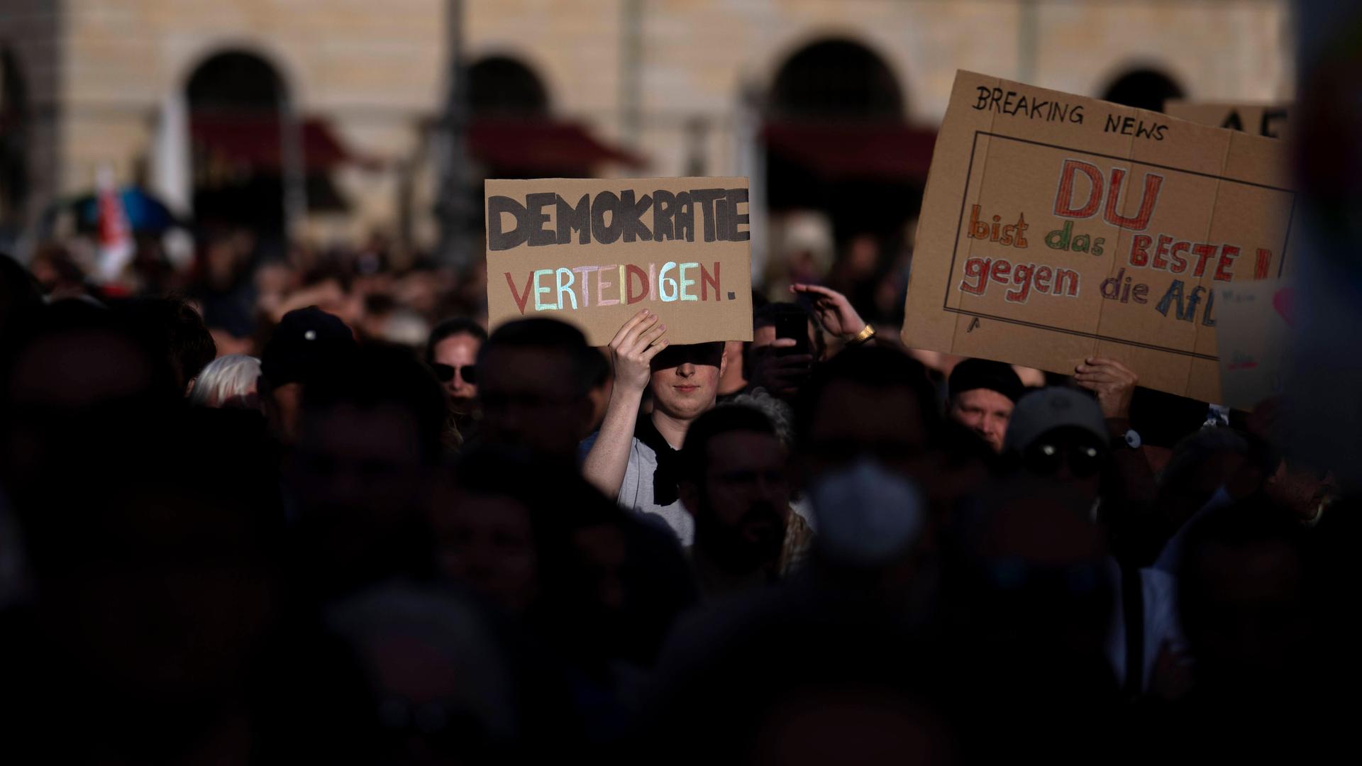 Ein Demonstrant steht bei der Kundgebung für Demokratie am 5. Mai 2024 vor dem Brandenburger Tor in der Menge hält ein mit Schild mit der Aufschrift "Demokratie Verteidigen" in die Höhe. 