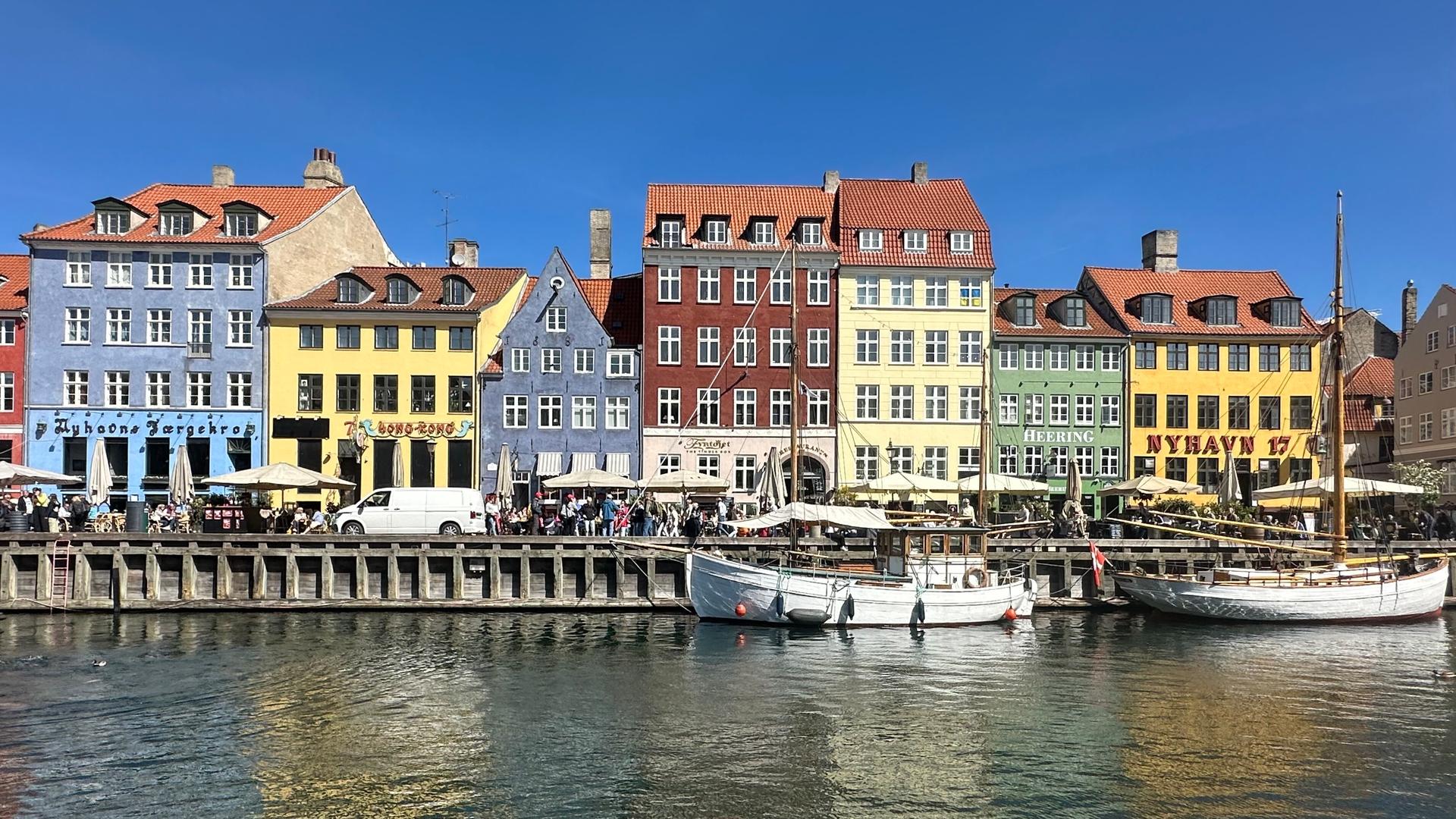 Mehrere bunte Häuser liegen vor einer Bucht. Dort liegen Segel-Schiffe vor Anker. Mehrere bunte Häuser liegen vor einer Bucht. Dort liegen Segel-Schiffe vor Anker.