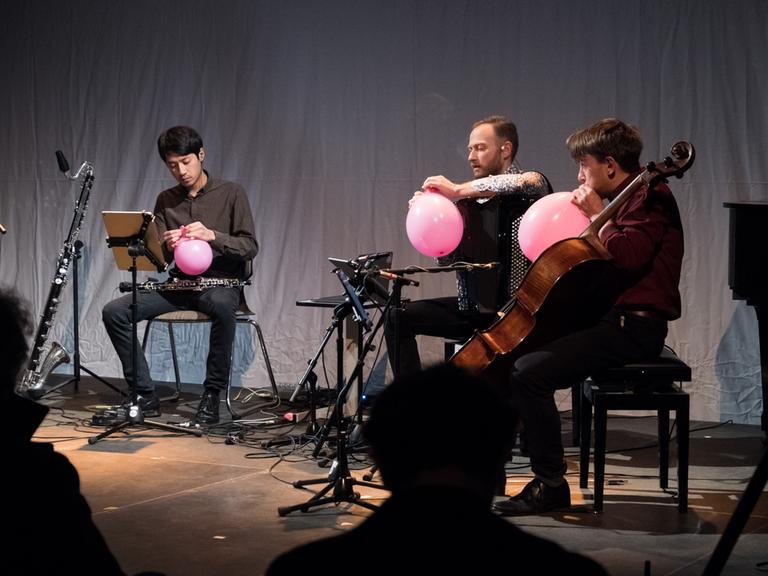Drei Musiker des Ensembles S201 sitzen auf der Bühne und hantieren mit rosafarbenen Luftballons