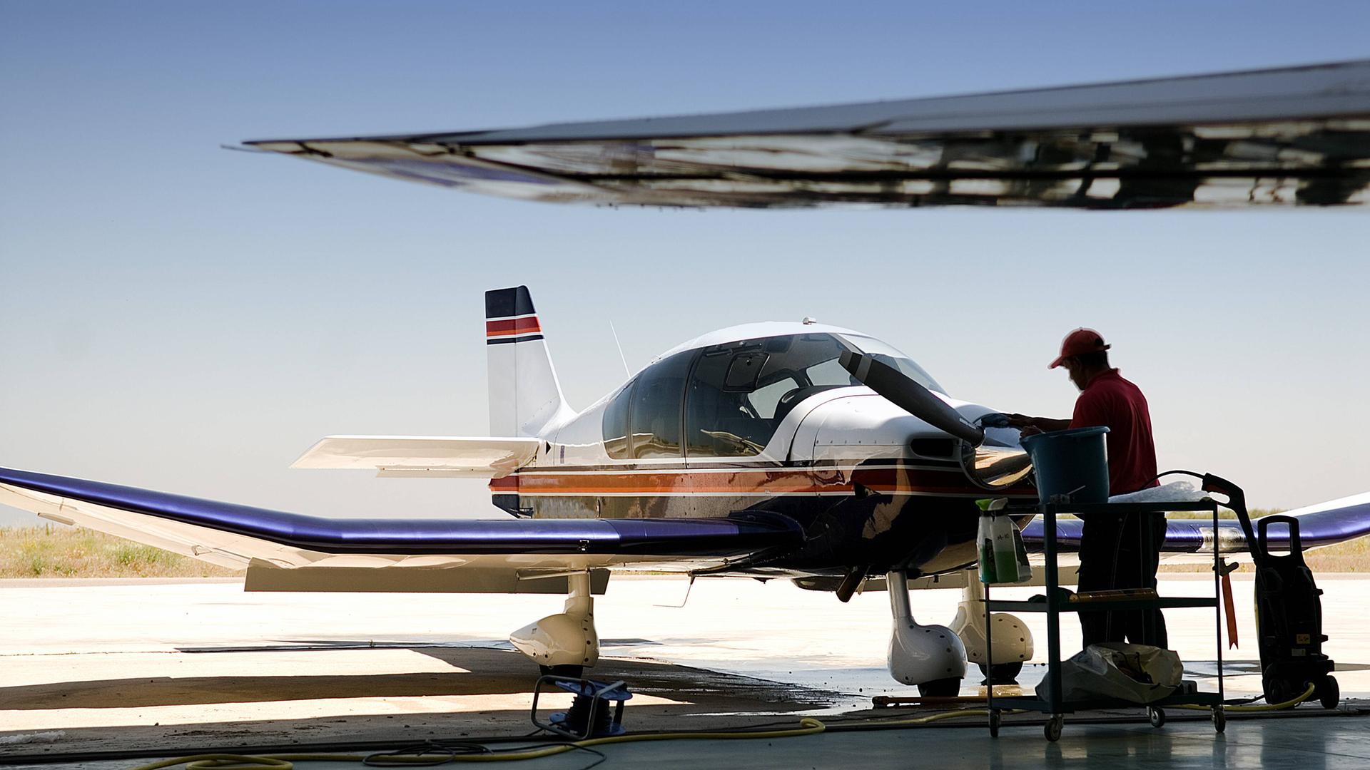 Side view of male employee in uniform cleaning jet airplane while standing on airfield during sunny day Copyright: xKavixSanchezx
