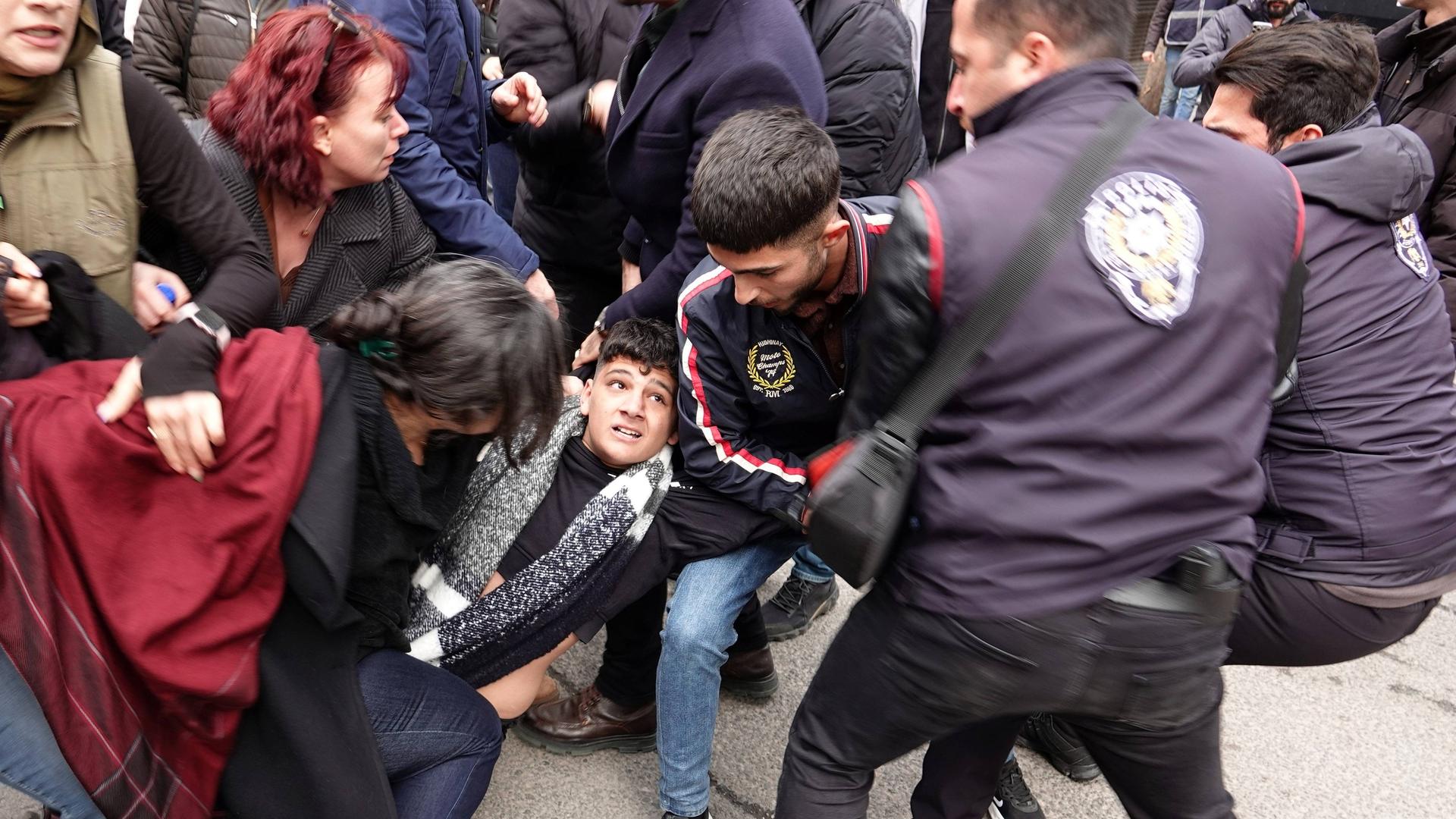 Rangelnde Menschen am Boden, die versuchen einen jungen Mann in der Mitte des Bildes vor der Polizei, rechts im Bild, zu retten.