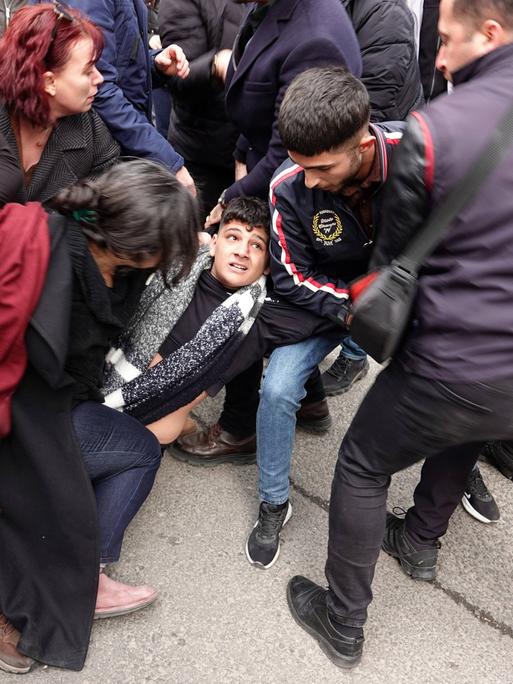 Rangelnde Menschen am Boden, die versuchen einen jungen Mann in der Mitte des Bildes vor der Polizei, rechts im Bild, zu retten.