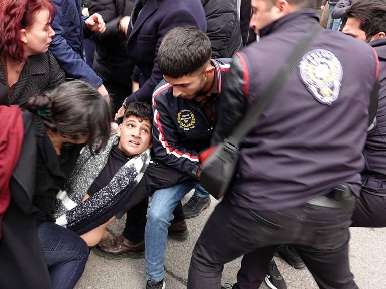 Rangelnde Menschen am Boden, die versuchen einen jungen Mann in der Mitte des Bildes vor der Polizei, rechts im Bild, zu retten.