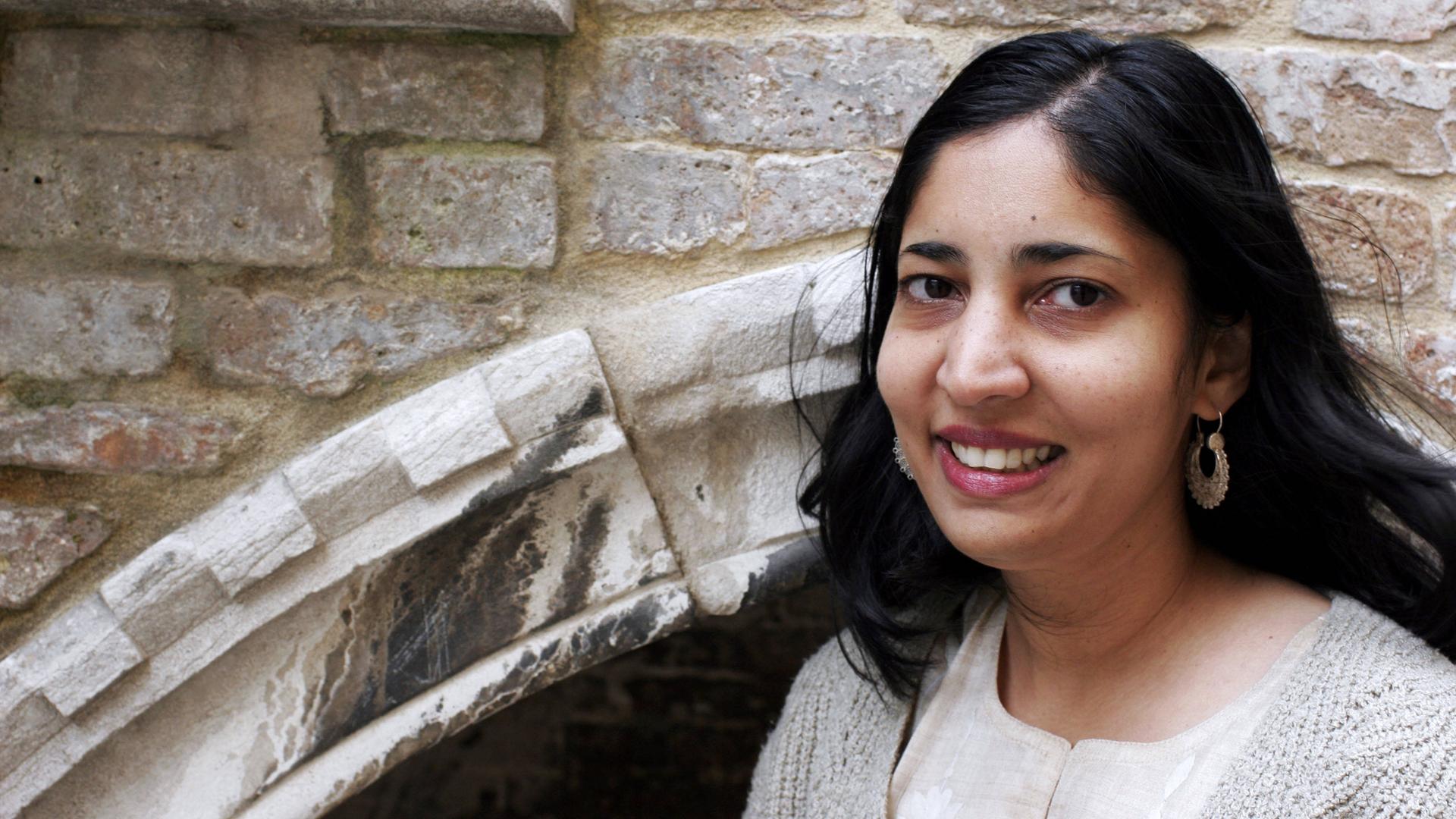 Die Schriftstellerin Kiran Desai steht lächelnd vor einem mittelalterlichen Mauerwerk. Die Schriftstellerin Kiran Desai steht lächelnd vor einem mittelalterlichen Mauerwerk.